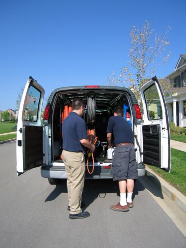 two workers unload a work van to do some vacuum jobs or clean a carpet in a suburban home.